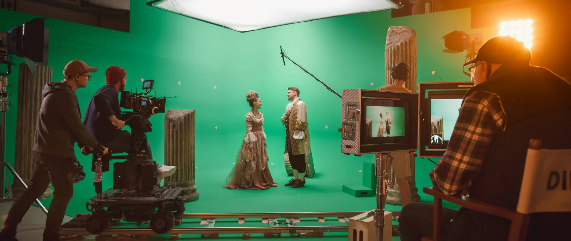 Virtual production studio setup with actors on a green screen, surrounded by production crew members, capturing footage for a film production.